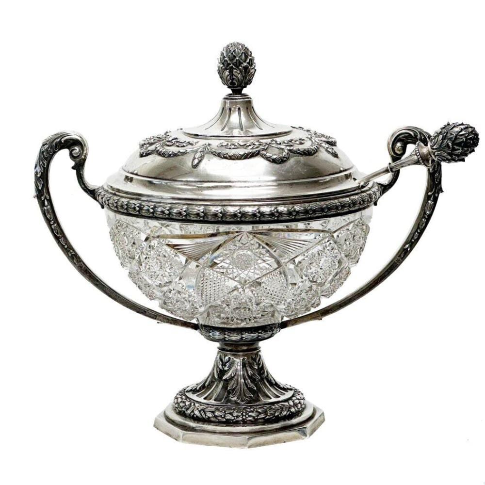 Silver-toned decorative punch bowl with faceted glass body and ornate leaf-and-grape border, with matching lid and handle ladle.