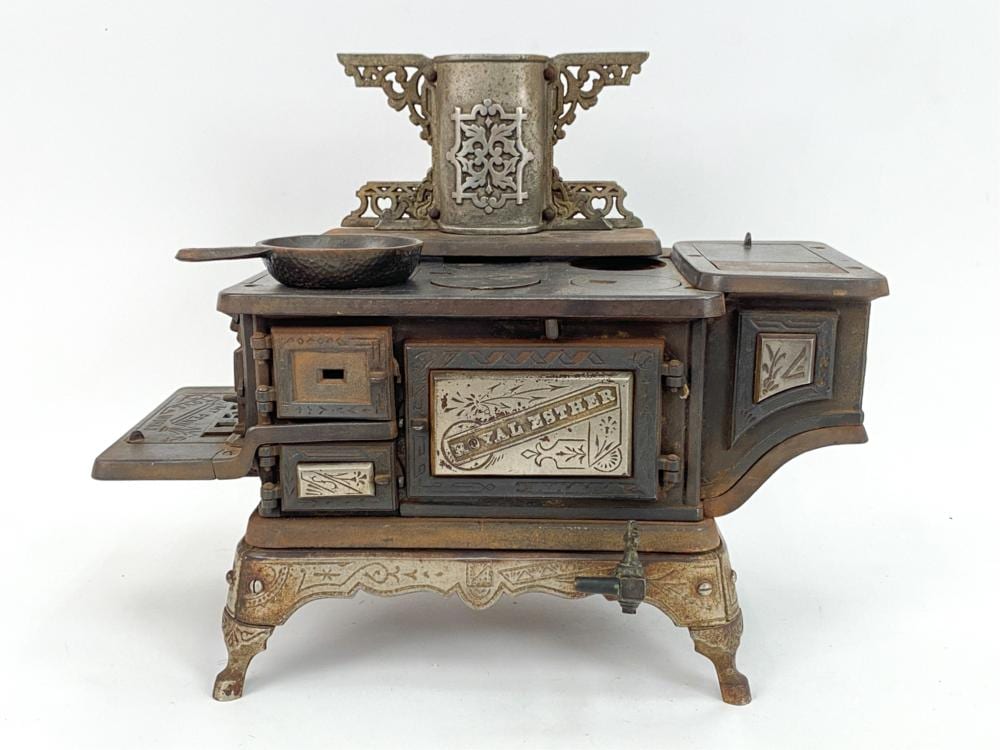 Cast iron toy stove with embossed doors, finials, and decorative panels; pot on top and side lids open.