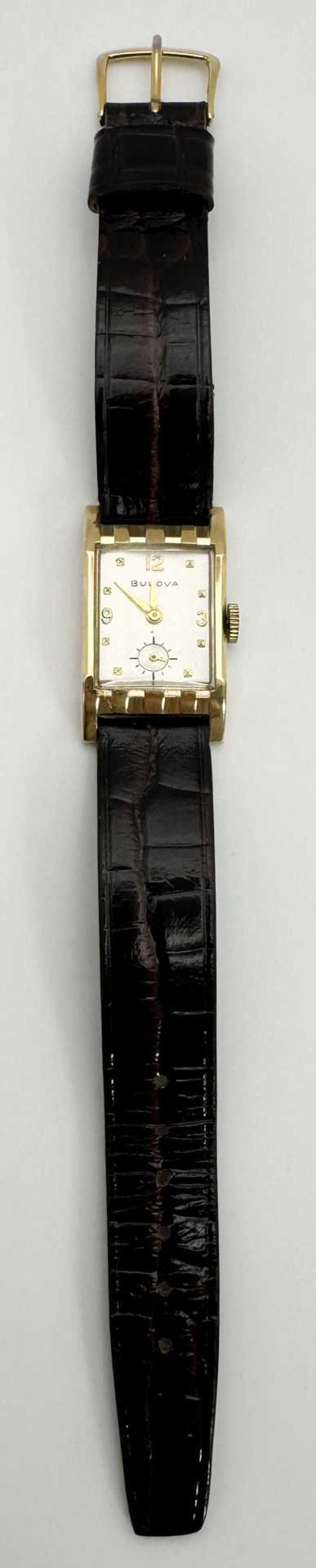Vintage wristwatch with a rectangular gold case, white dial, and black leather strap.
