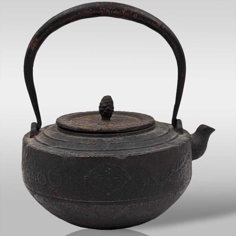 Cast iron kettle with arched handle and round lid finial, shown against a light background.