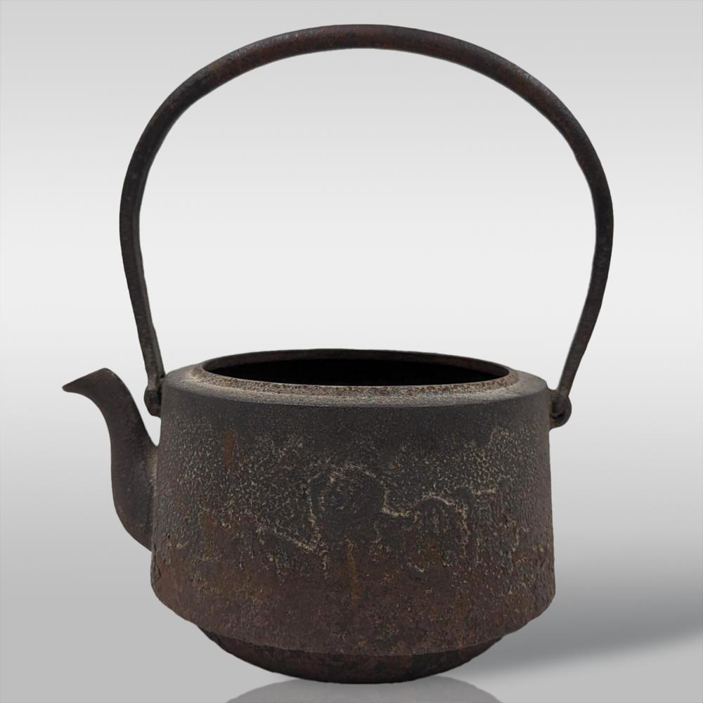 Antique-style cast iron kettle with arched handle and spout, dark brown with textured surface and rusted patina.