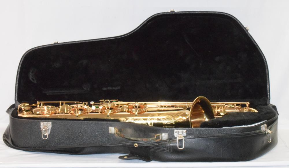 Gold-colored baritone saxophone resting in a black case with the bell facing right; case lid open and velvet-lined interior visible.