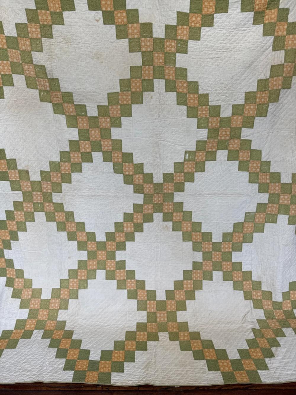Close-up of a white quilt with a repeating star pattern made of green and tan fabric blocks.