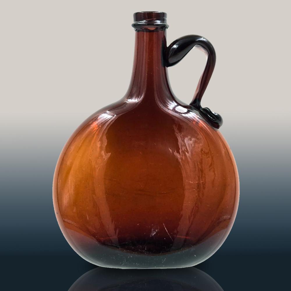Amber glass bottle or flask with a round body, short neck, and applied handle, photographed against a gray background.