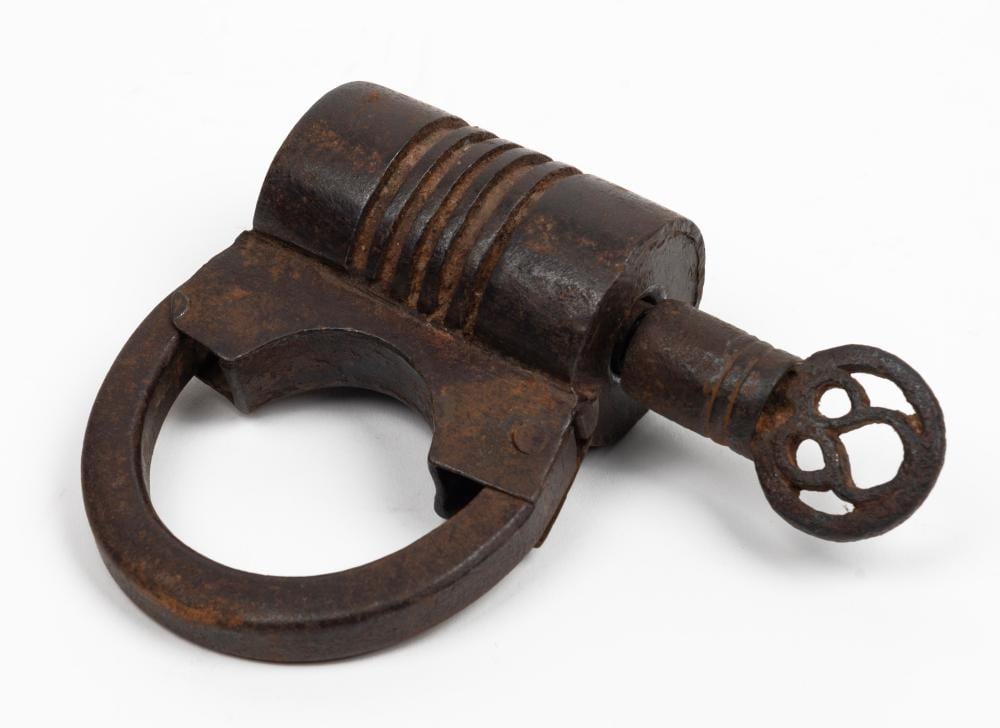Rusty antique iron padlock with a ring-shaped shackle and a short cylindrical key attached, shown on a white background.