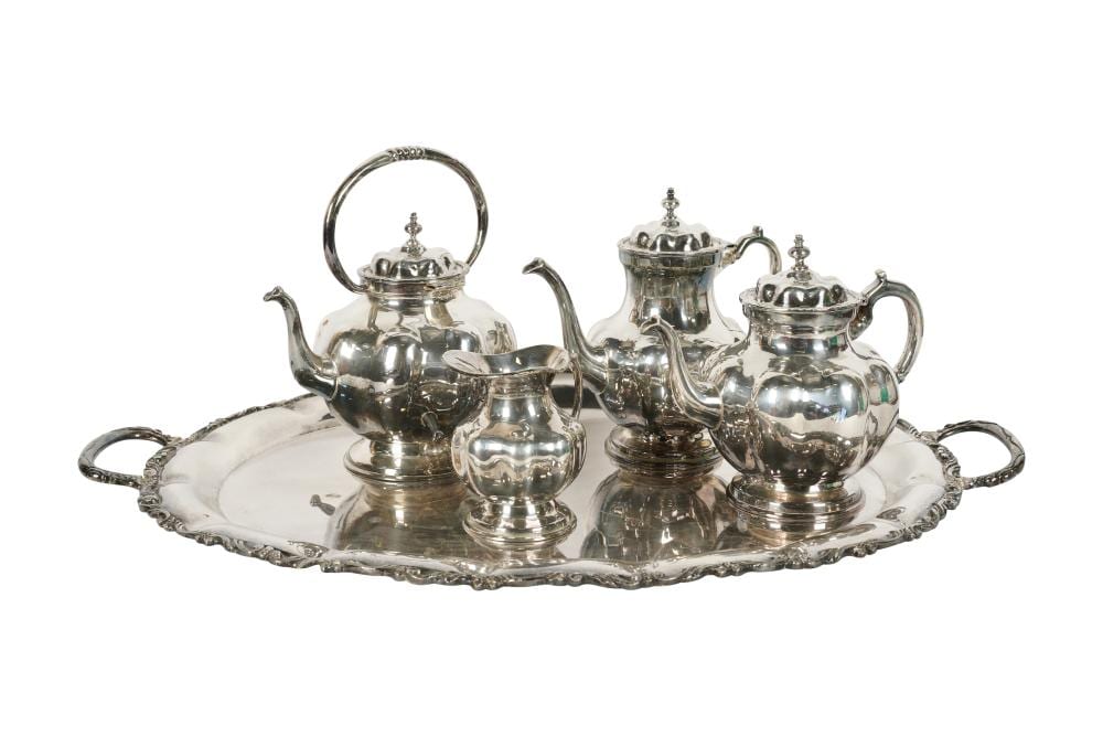 Silver tone tea service with teapot, kettle, sugar bowl, creamer, and tray set on a white background.