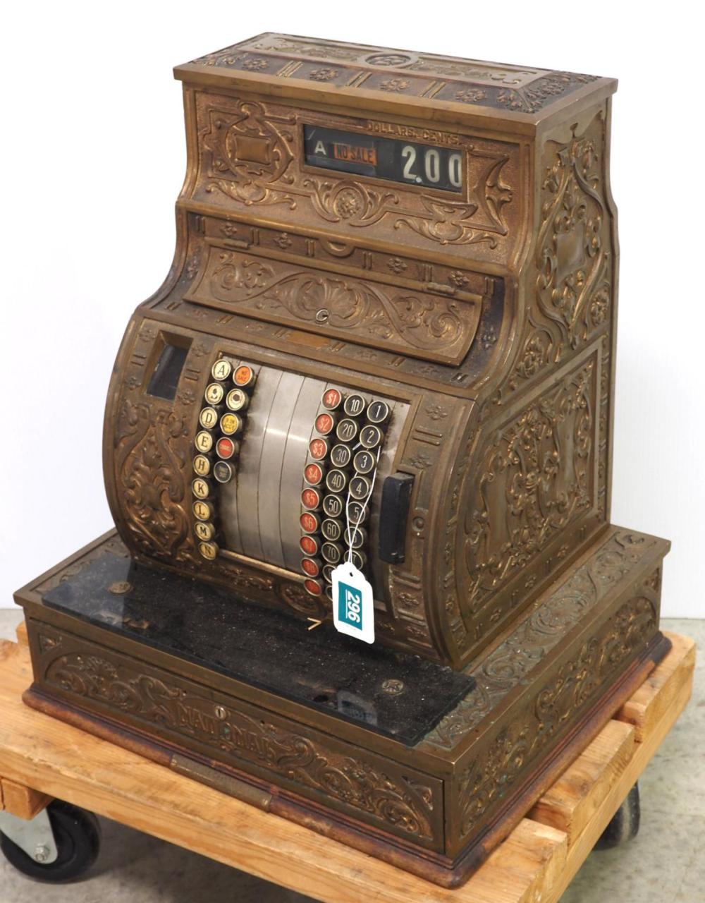 Brass antique cash register with ornate embossed panels, coin slots, and a front register window showing “200” for dollars.
