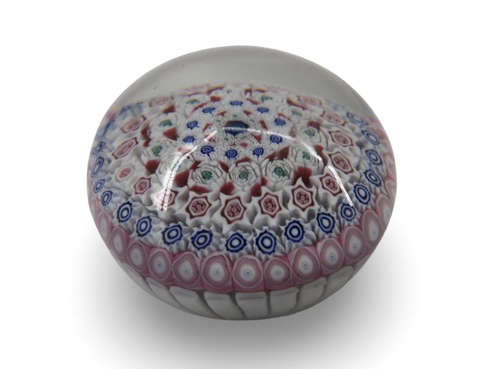 Round glass paperweight with millefiori-style flowers and blue geometric dots under a clear surface.