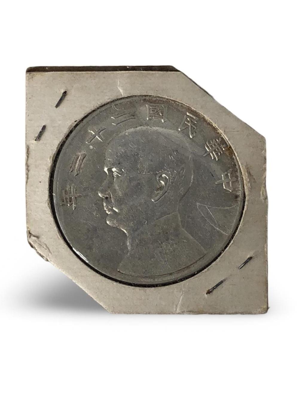 Close-up of a dark metal coin with Chinese characters and a profile portrait at center, shown inside a square plastic holder.