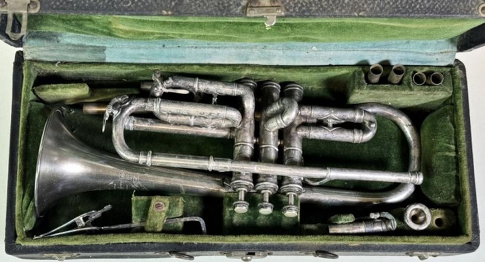 Silver-colored trumpet with valves and leadpipe lying inside a green fabric case, shown from above.