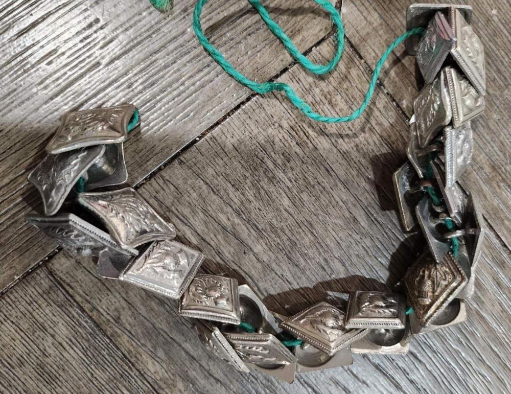 Close-up of several antique metal military-style buttons with green thread attached, laid on a wooden surface.