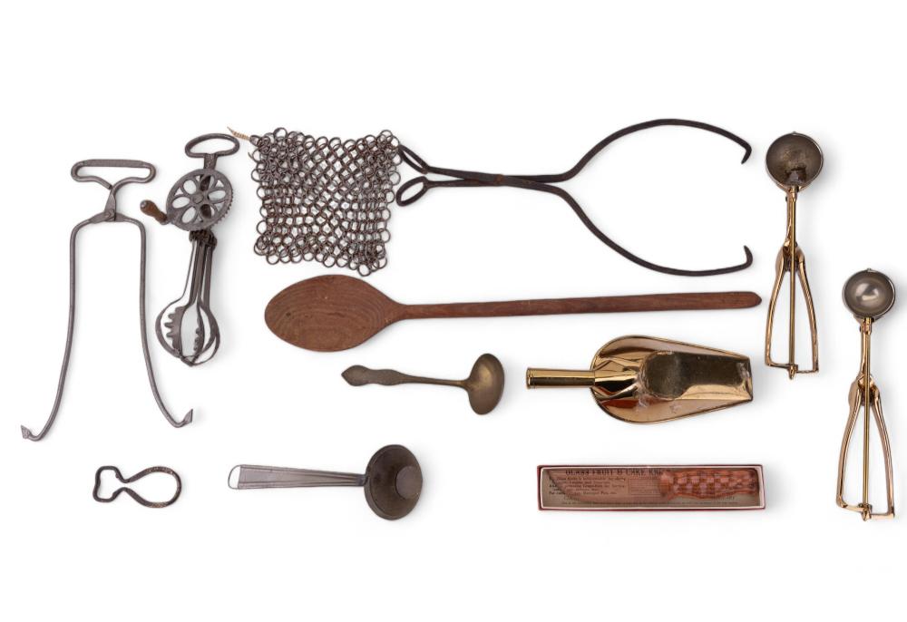 Assorted antique-style kitchen utensils including a wire mesh strainer, wooden-handled ladle and scoop, and brass tools on a white background.