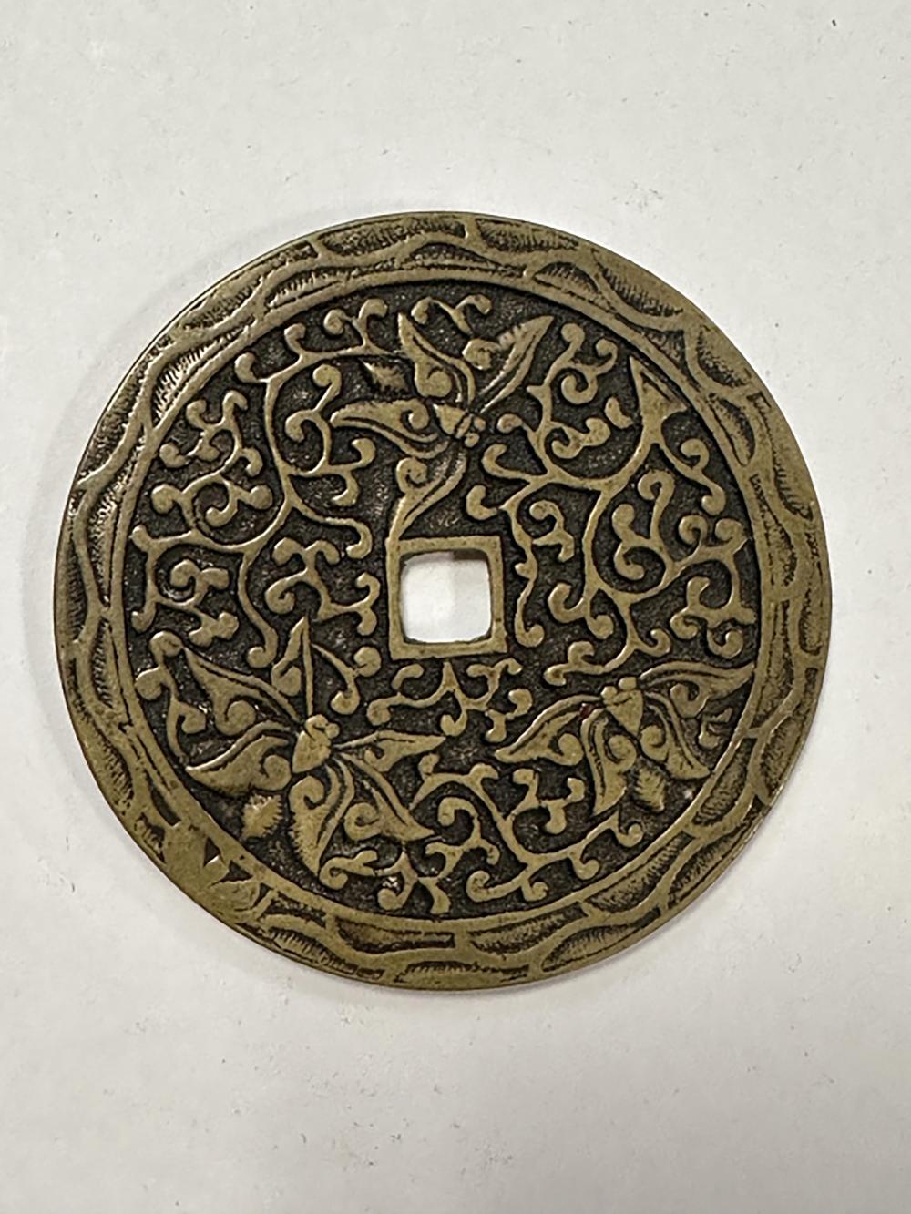 Close-up of an antique-style bronze coin with ornate engraved patterns and a central square-like motif.
