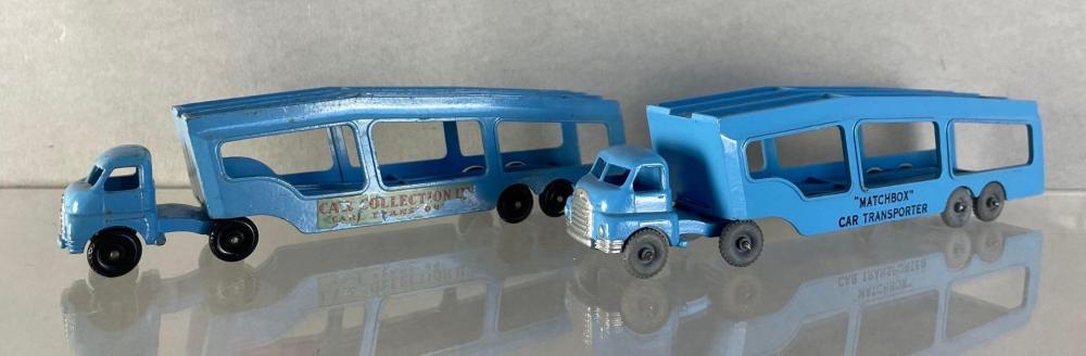 Two blue die-cast matchbox-style car transporter trucks with large cabovers, shown side-by-side on a reflective surface.