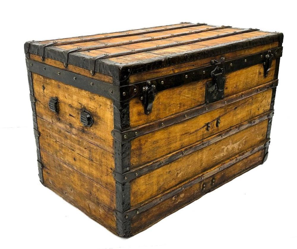 Brown wooden steamer trunk with black metal corner guards, rivets, and leather strap handles on a white background.