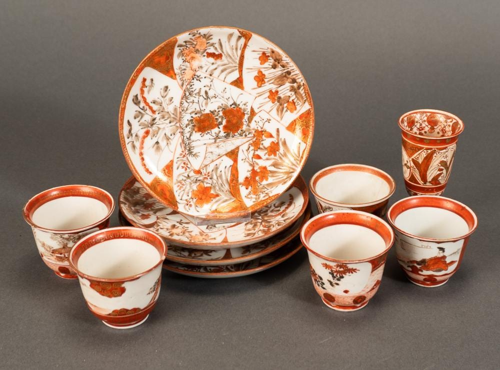 Set of Japanese-style porcelain cups and saucers with orange-red rims and floral designs, arranged on a gray background.