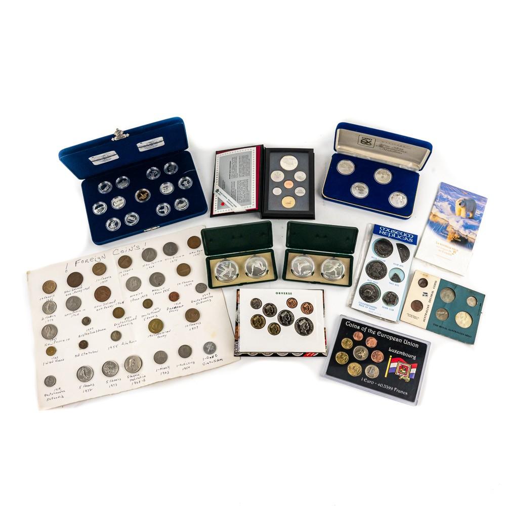 Assorted coin sets in blue cases and card sleeves, showing various commemorative coins and labels on white background.