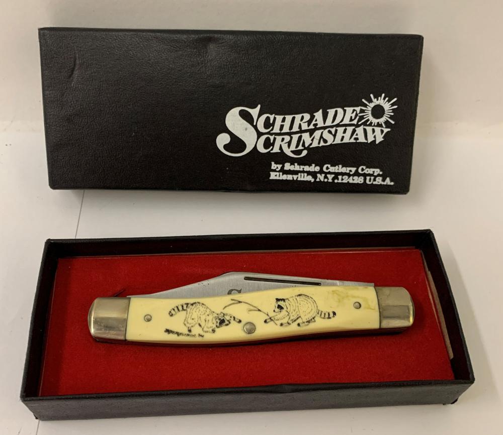 Schrade Scrimshaw-style pocket knife in a black presentation box with red interior, showing an ivory-colored handle with etched figures and metal blades.
