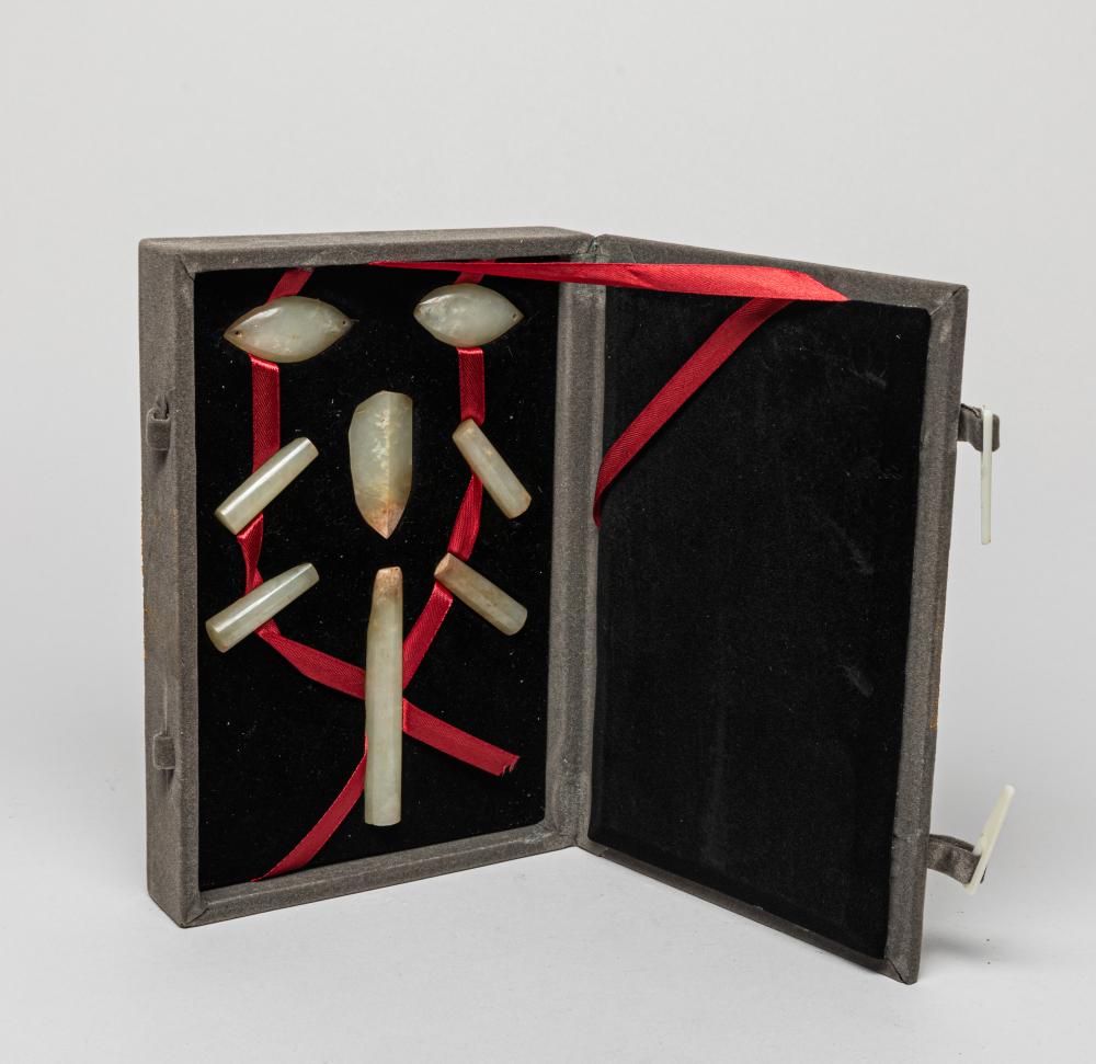 Open black display case showing several pale jade-like carved pieces attached with red ribbon.