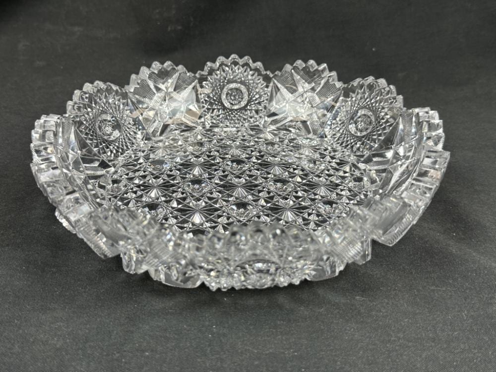 Clear cut-crystal shallow bowl with diamond and fan facets, viewed from above against a dark background.