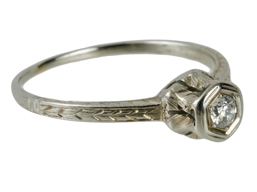 Close-up of a white gold diamond wedding ring with a round center diamond and engraved band.