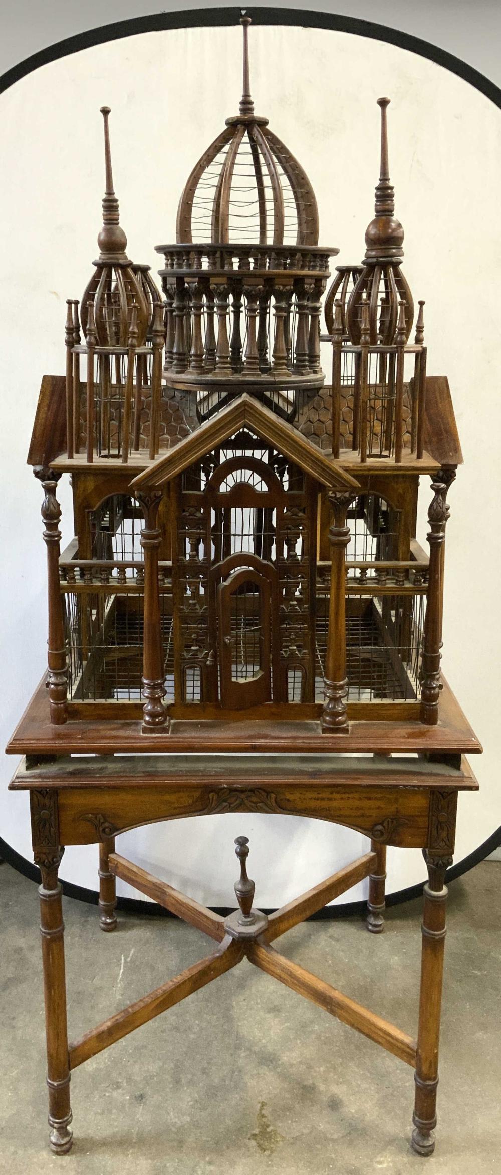 Wood birdcage display with multiple domed top sections, decorative finials, and a small house-like front panel on a pedestal stand.
