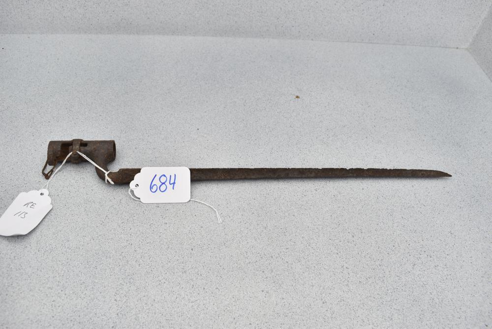 Rusty metal bayonet with a long blade, shown on a light gray surface, with tag labels attached near the hilt.