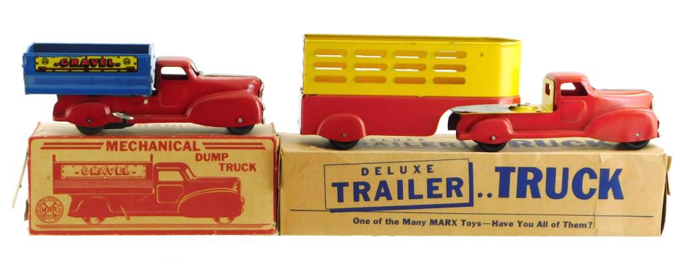 Red mechanical dump-style toy truck with blue sign reading "GRAVEL," shown with its cardboard box and a second truck in the background.