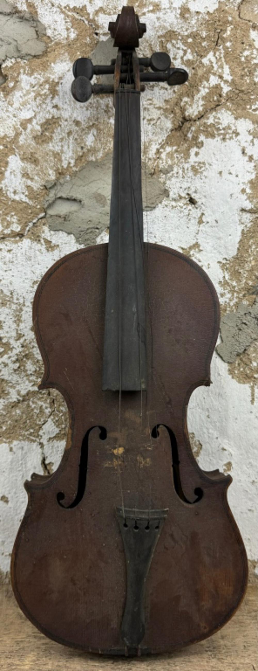 Front view of an antique-style violin with dark wooden body, curved shoulders, and four tuning pegs against a stone wall background.