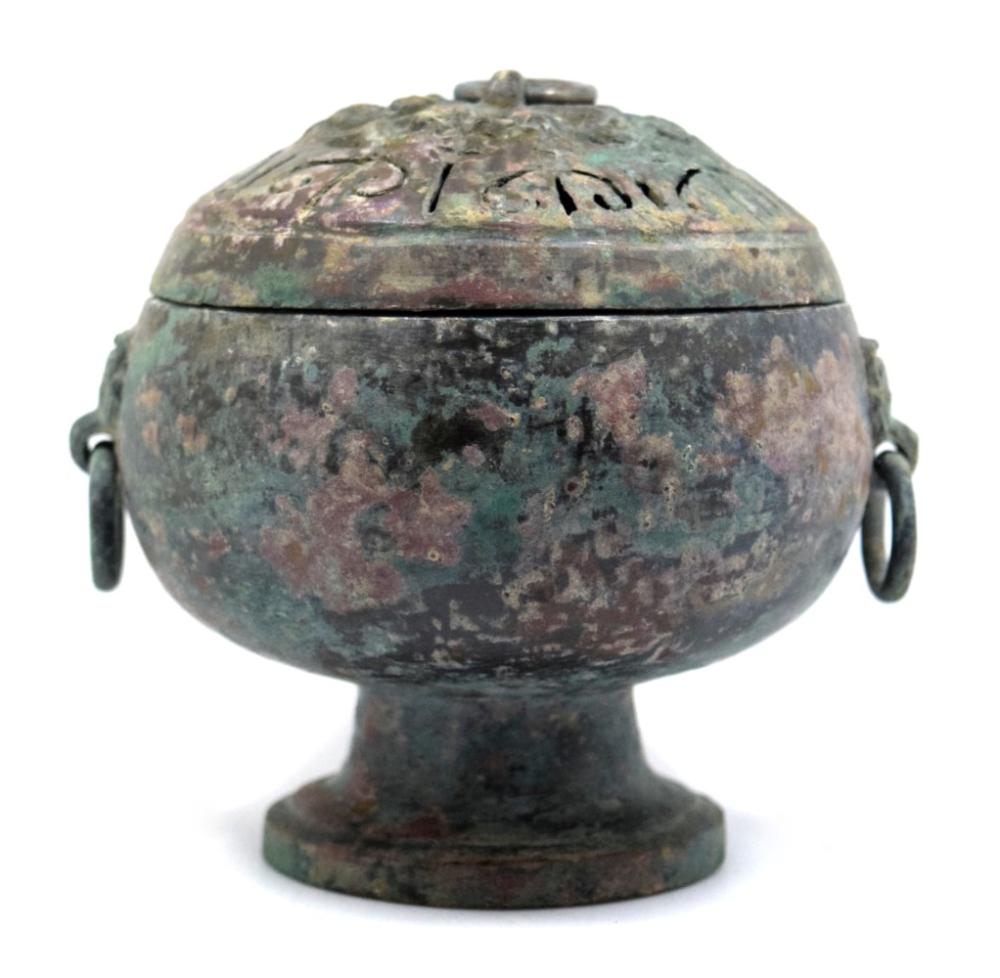 Bronze incense burner with a domed lid, two side handles, and green patina, shown centered on a light background.
