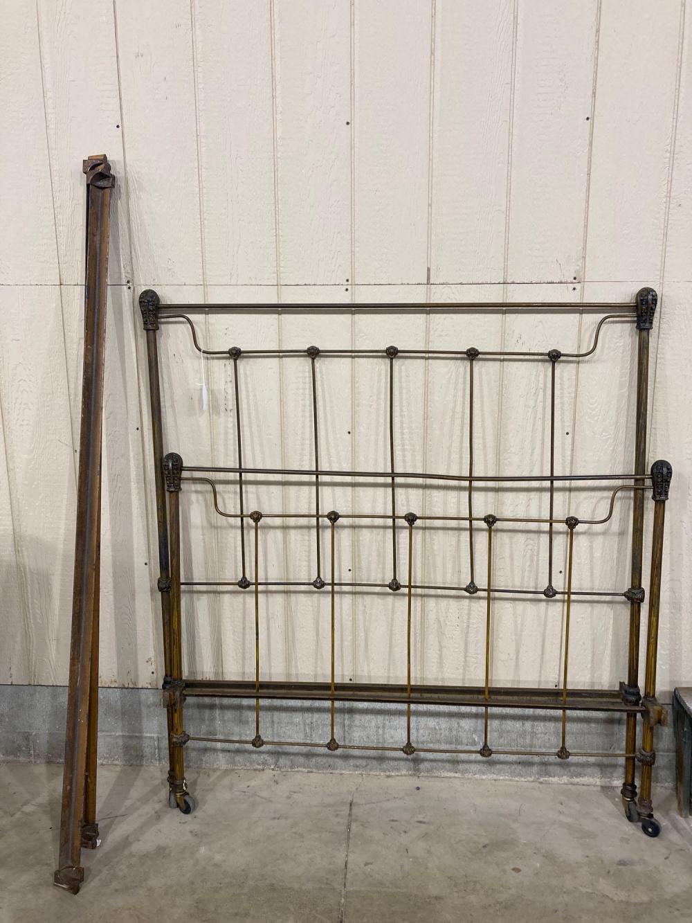 Brass full-size bed frame with curved headboard and footboard rails and vertical metal spindles, shown indoors against a wall.
