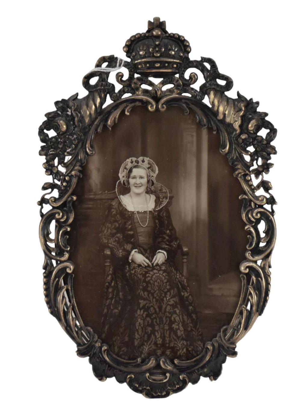 Oval antique picture frame with ornate scrollwork and a small crown finial, holding a vintage portrait photo of a young woman.