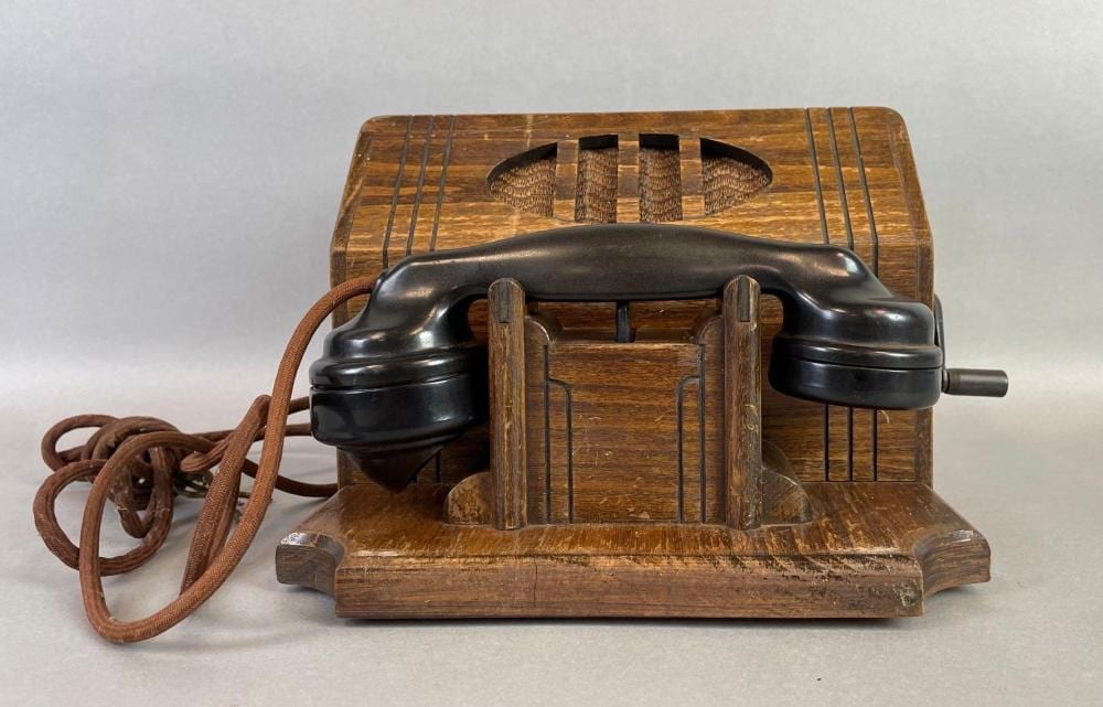 Vintage tabletop crank telephone with a dark handset and wooden base, front view with visible cord.