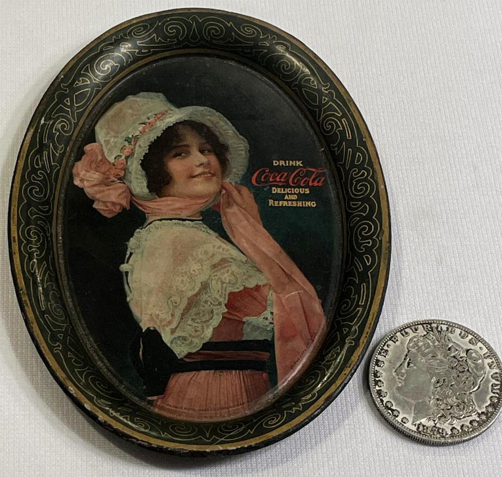 Oval metal tip tray with a vintage Coca-Cola Betty girl illustration wearing a bonnet and holding a drink, surrounded by decorative scrollwork border.