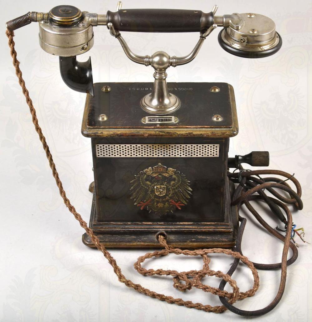Antique-looking German crank telephone with two curved metal handsets, brass dial plate, and coiled cord on a black base.