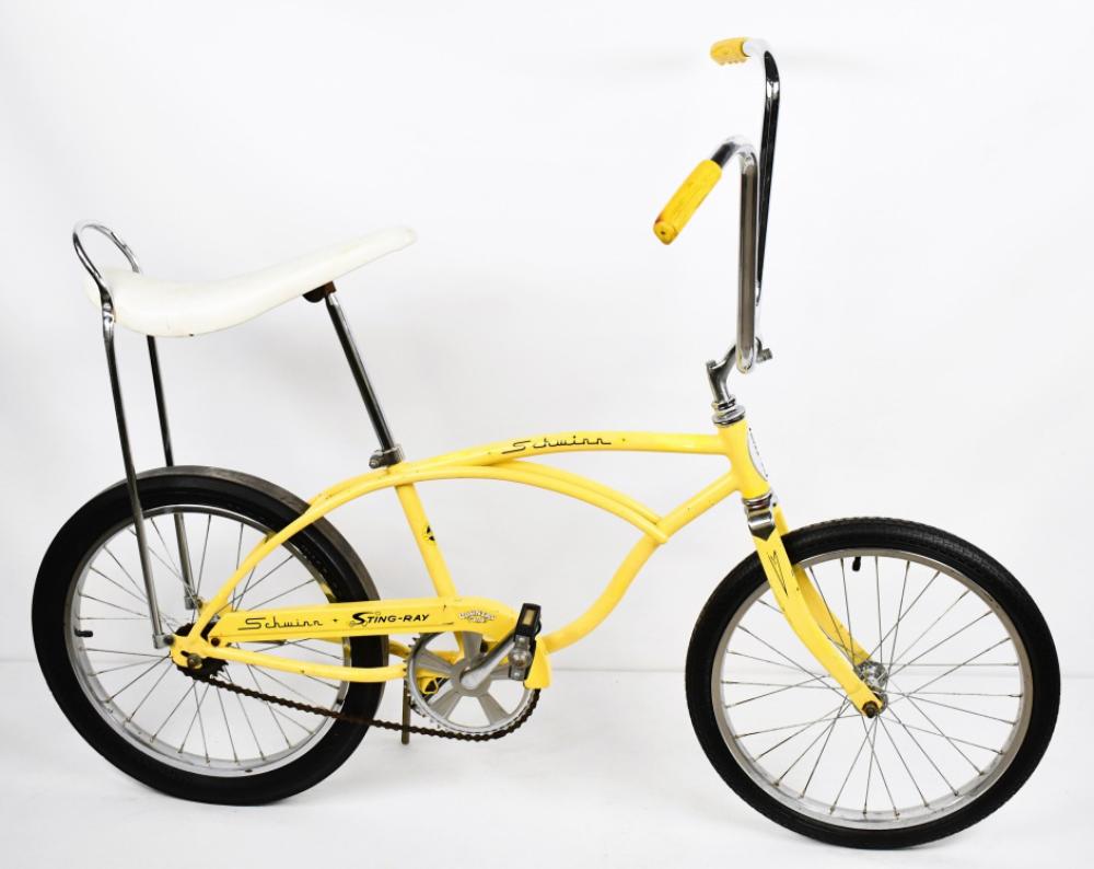 Yellow vintage bicycle with white seat, black tires, and chrome handlebars, shown in side view against a white background.