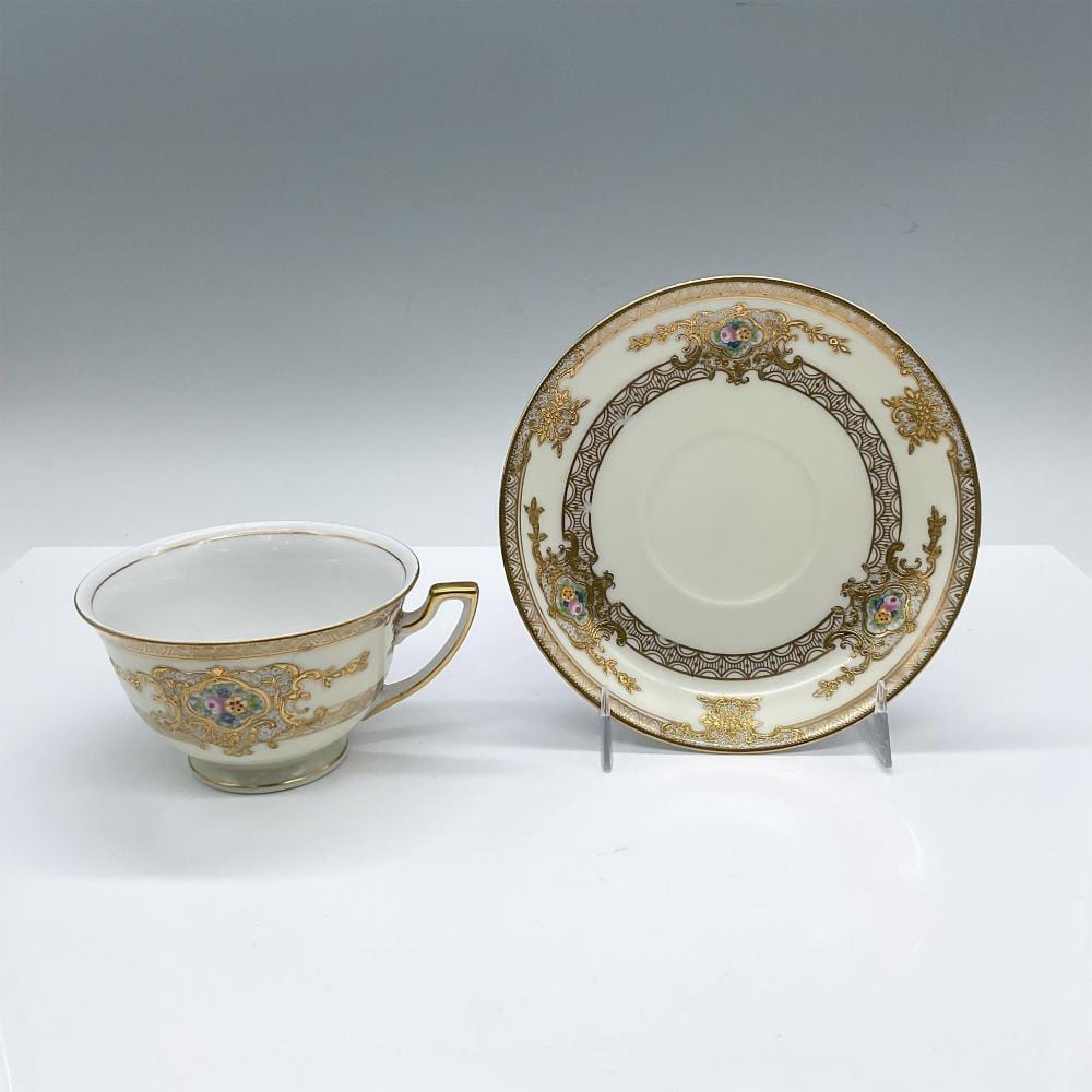 Porcelain teacup with gilded gold trim and floral medallion pattern, shown with a matching saucer on display stands.