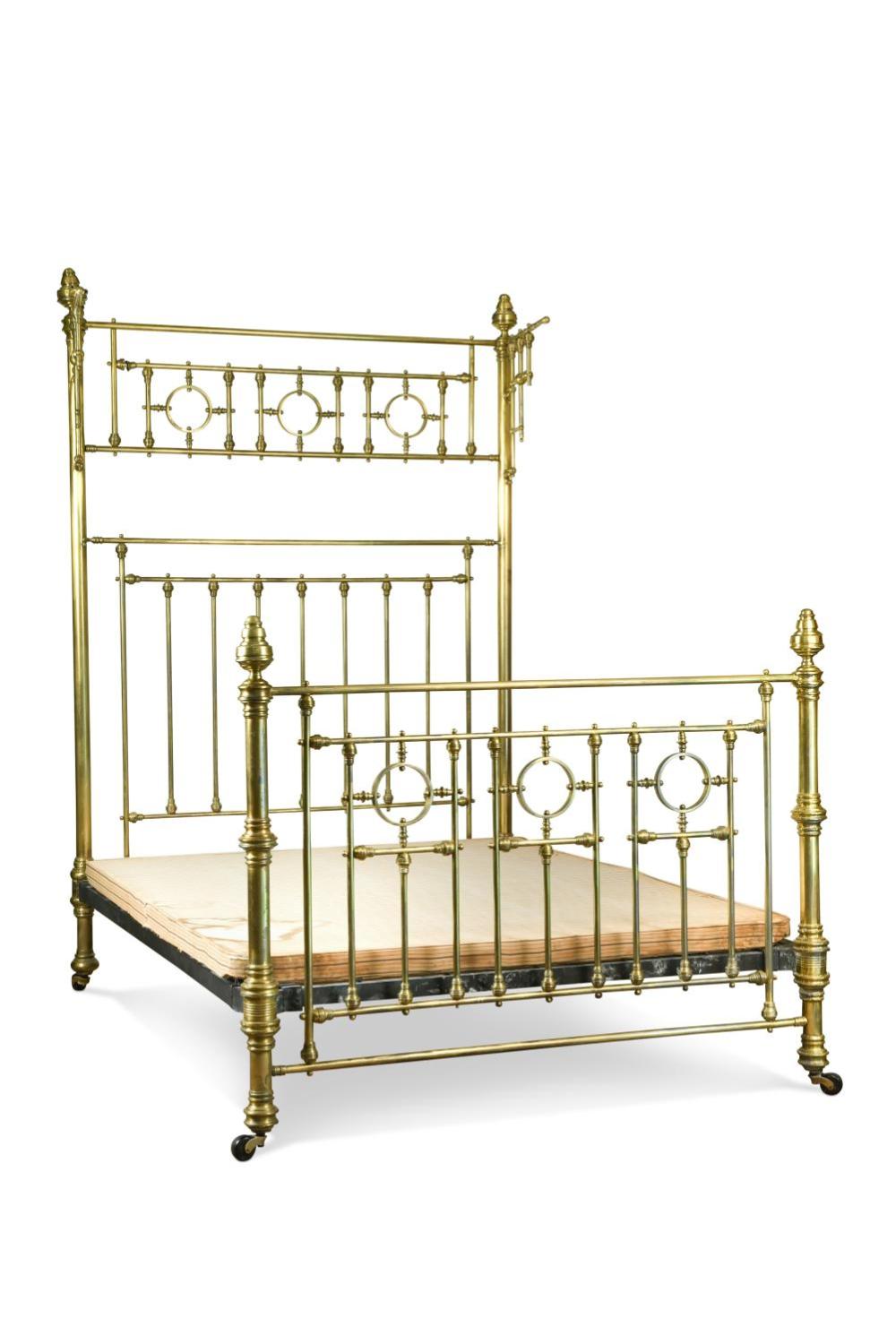 Brass-colored metal double bed frame with turned posts, finials, and vertical spindle rails supporting a light wooden mattress platform.