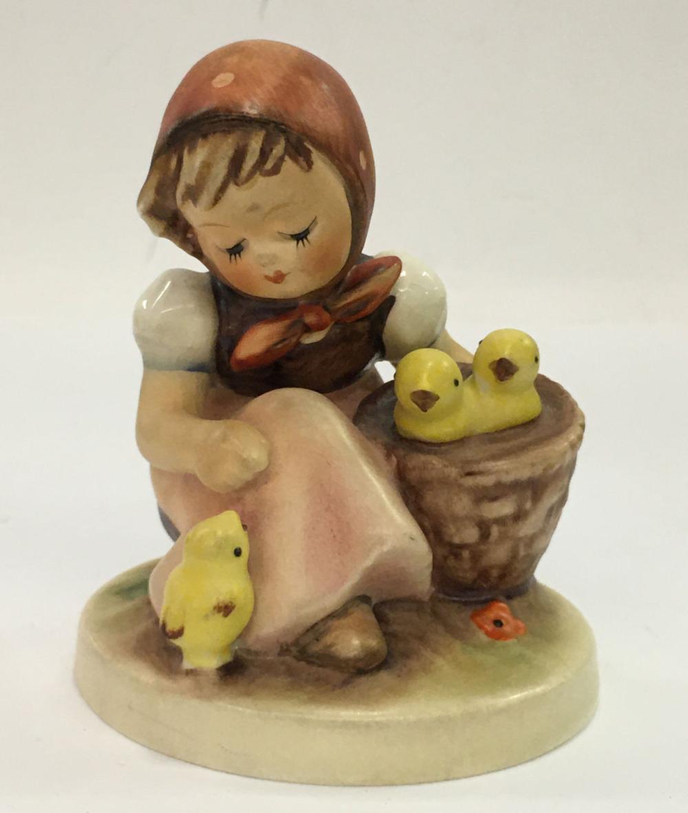 Ceramic figurine of a child in a bonnet holding a small book, seated with three yellow chicks on a base.