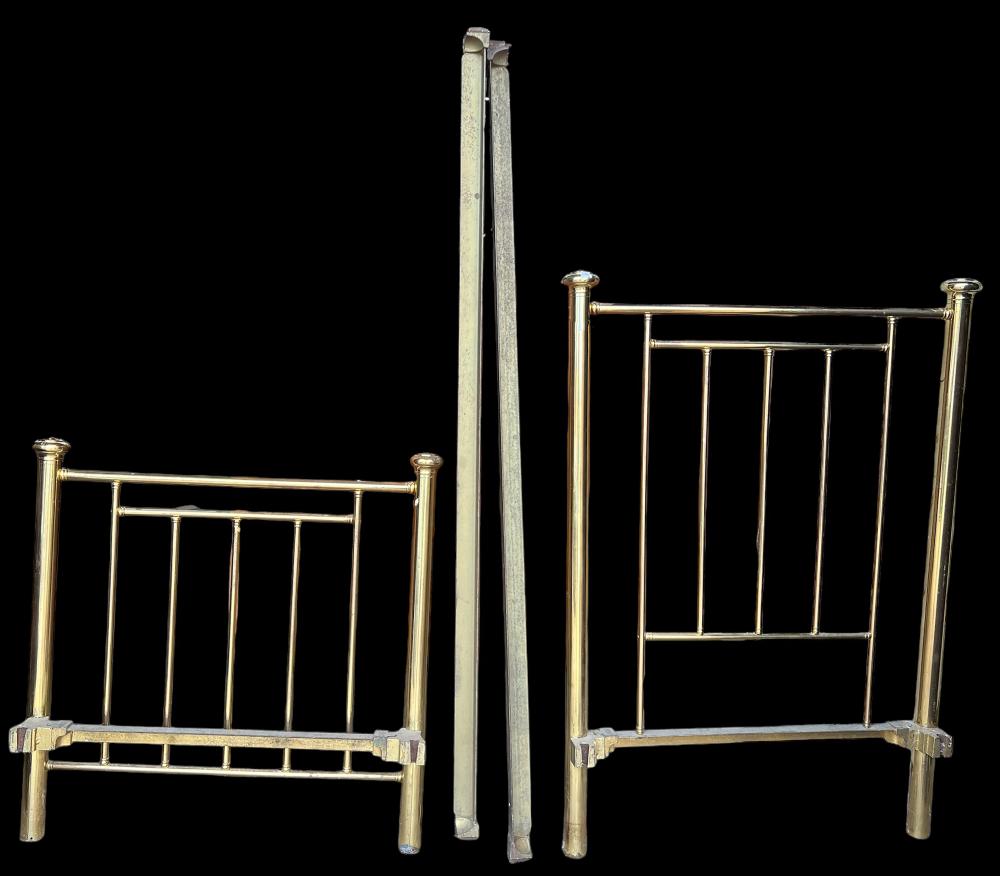 Pair of small brass metal twin bed frames shown side by side against a black background, with vertical slats and posts.