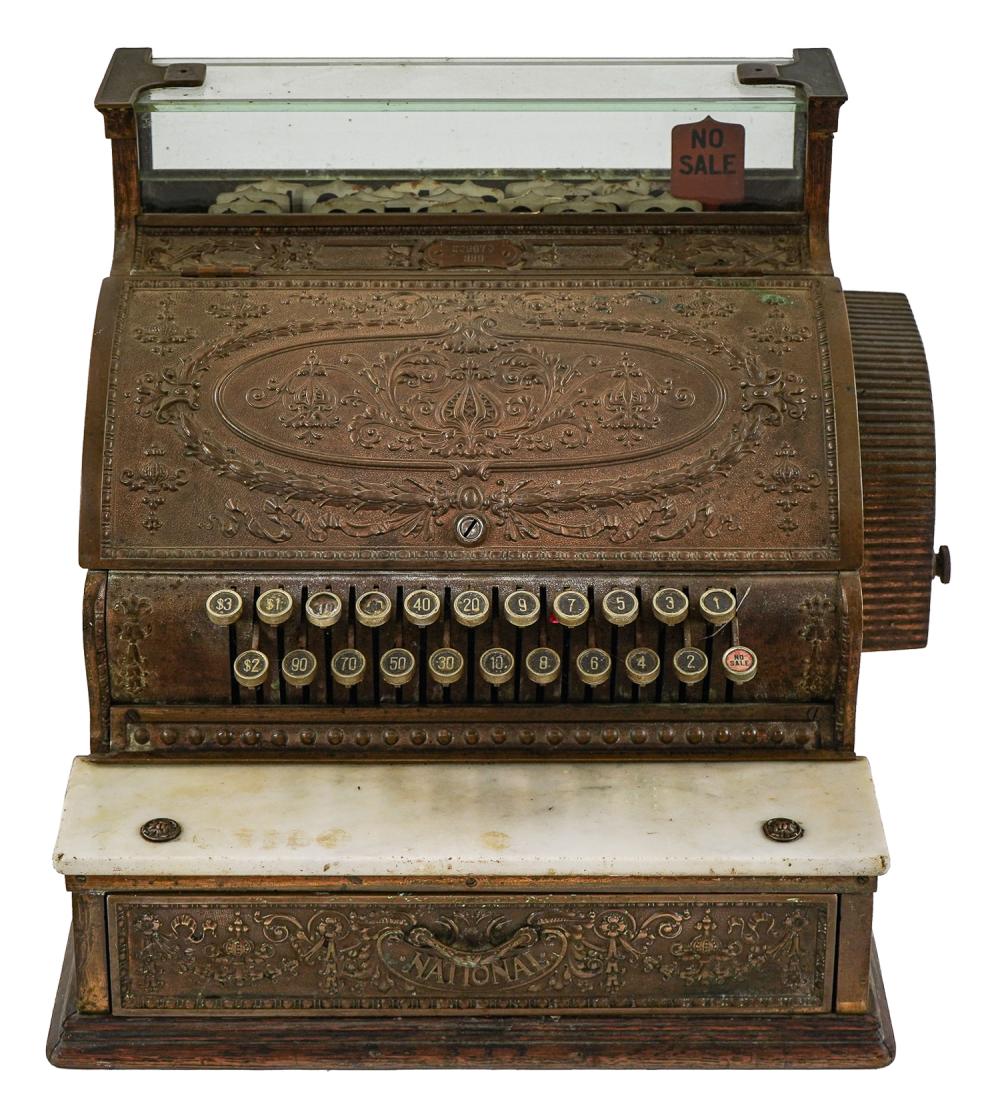 Brass cash register with ornate front panel, numbered coin-like keys, and a row of price/value dials.