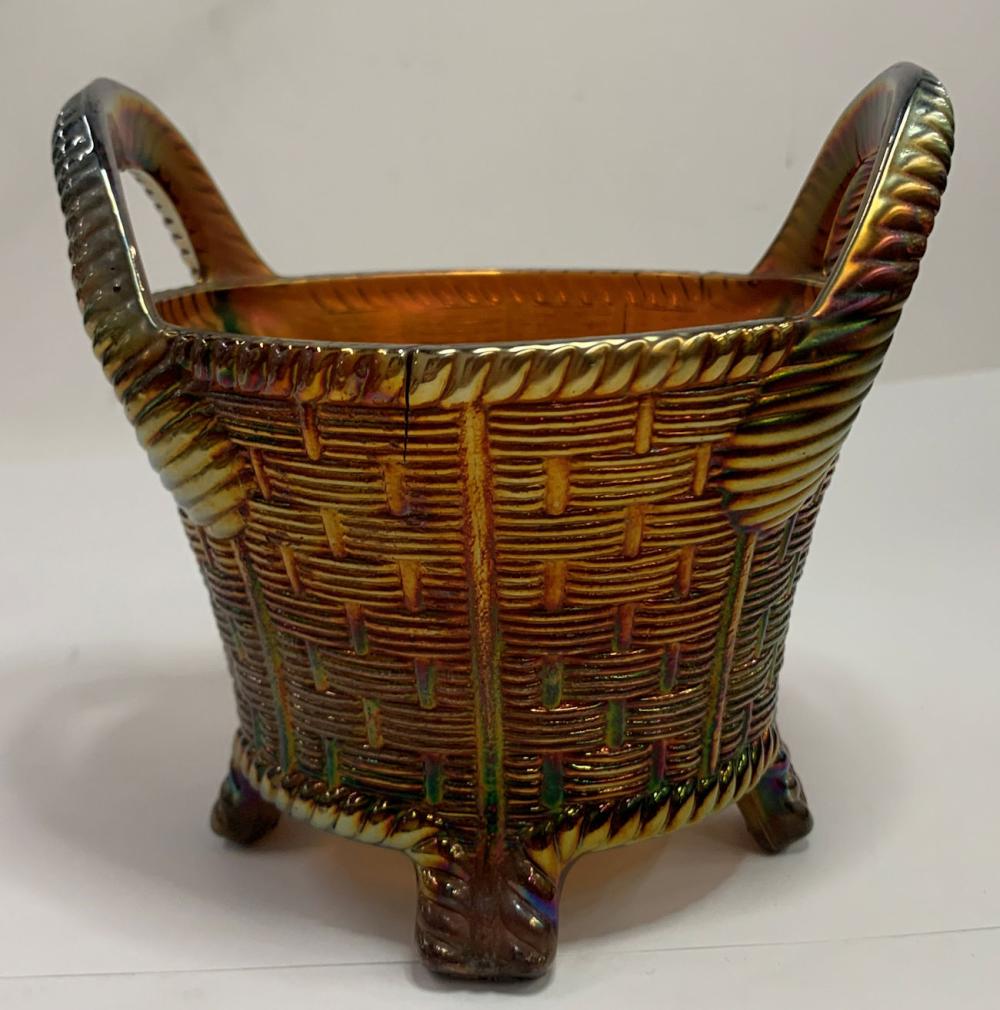 Carnival glass basket with an amber center and dark molded pattern, standing on small feet with flared handles at both sides.