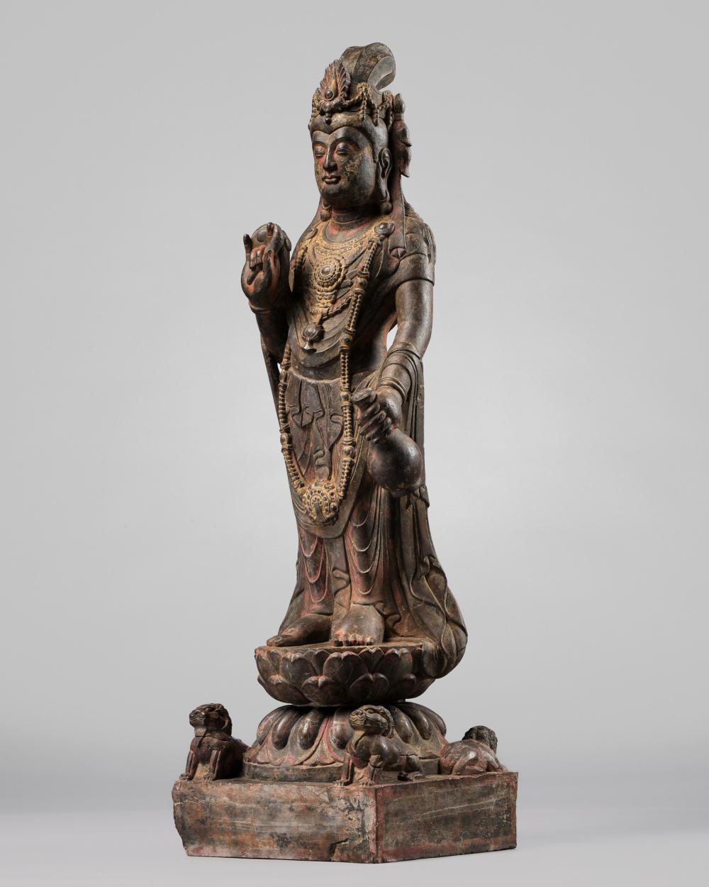 Full view of a painted stone Buddhist figure standing with one hand raised, wearing a crown and holding a small object in the other hand.