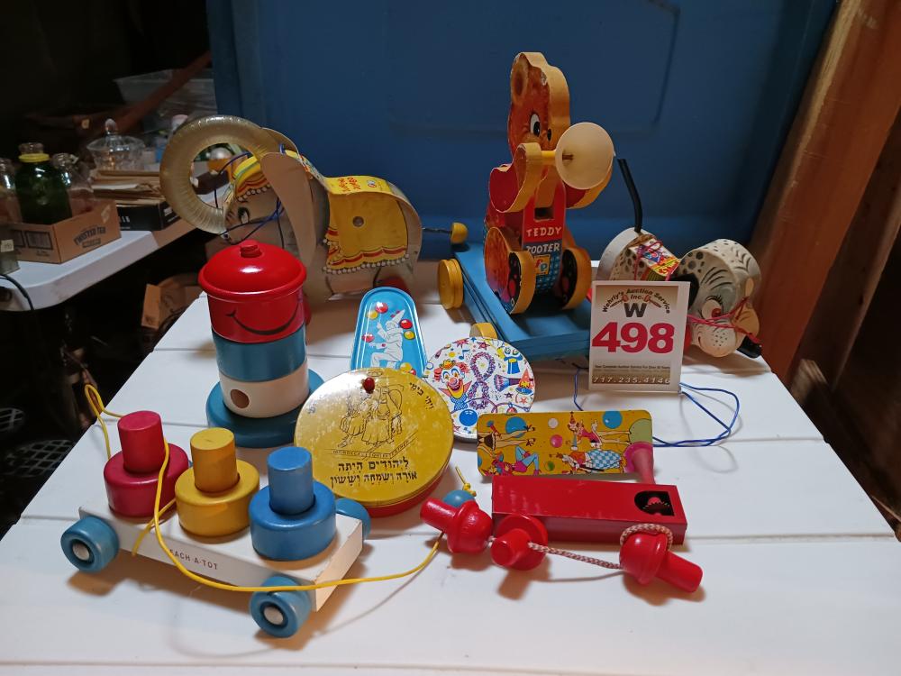 Assorted colorful vintage-style pull and push toys, including a red animal pull toy, a blue musical-style toy, and a teddy-bear pull toy, on a table.