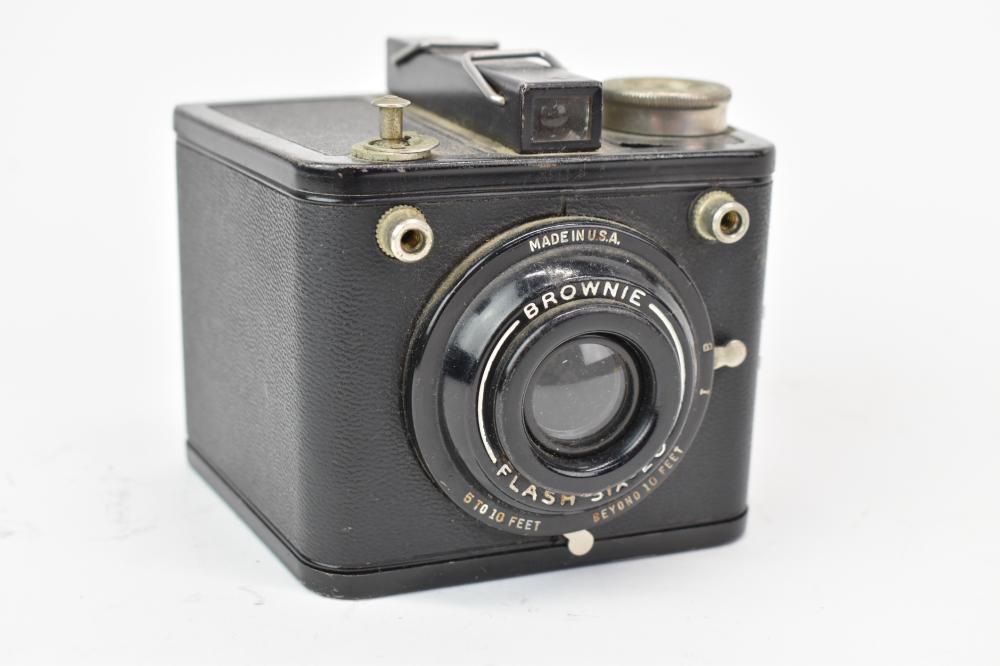 Black Kodak Brownie camera with a circular lens front, top viewfinder housing, and metal reels on a white background.