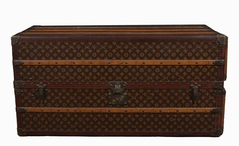 Brown monogram-pattern steamer trunk with metal corner guards and buckles, shown front view against a white background.