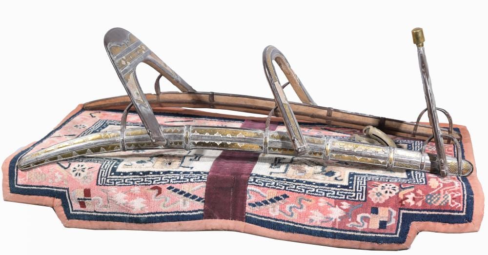 Antique camel saddle with patterned textile pad and metal stirrups over a wooden frame