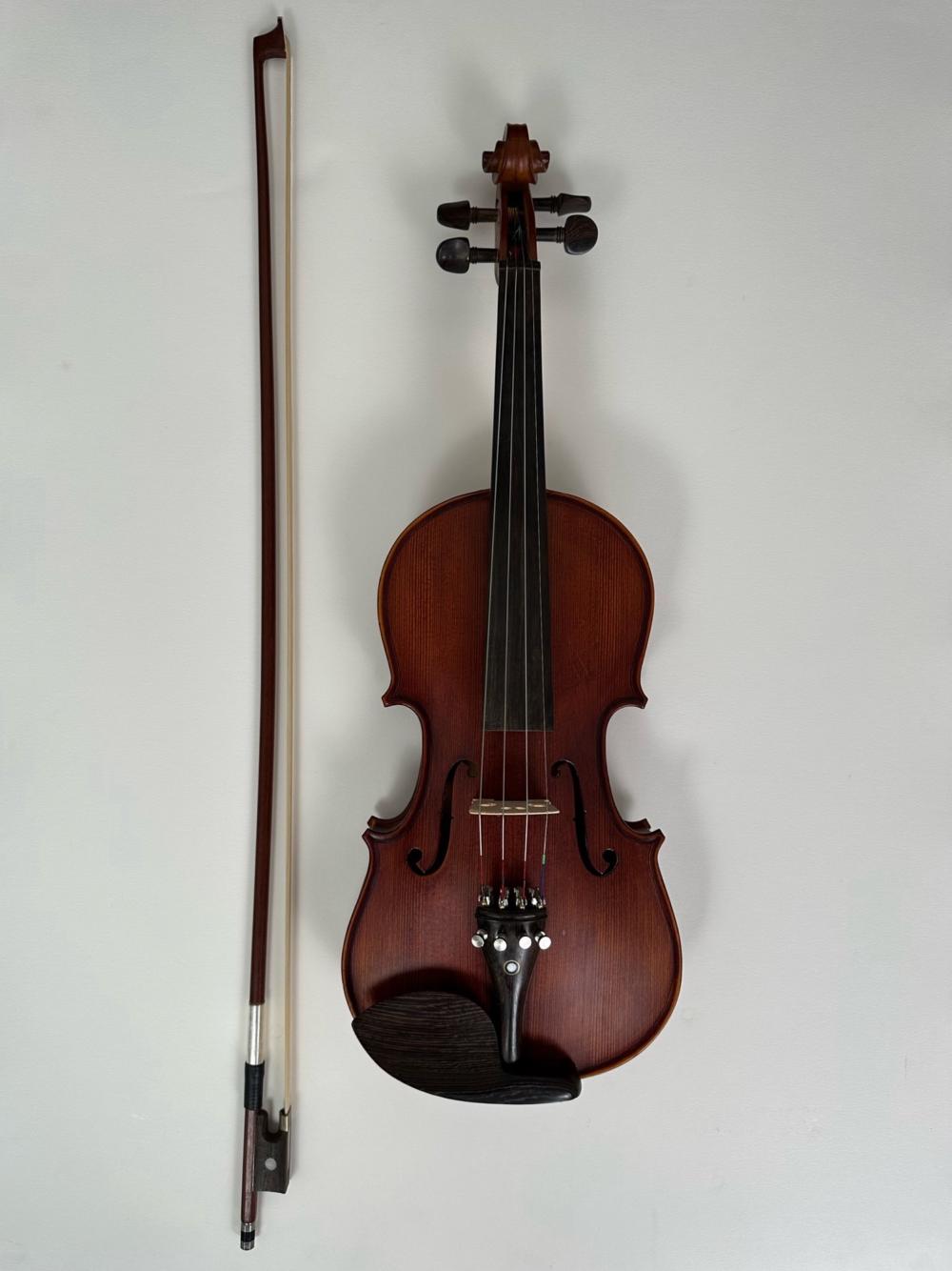 Brown violin with four strings and a bow displayed against a plain light background.