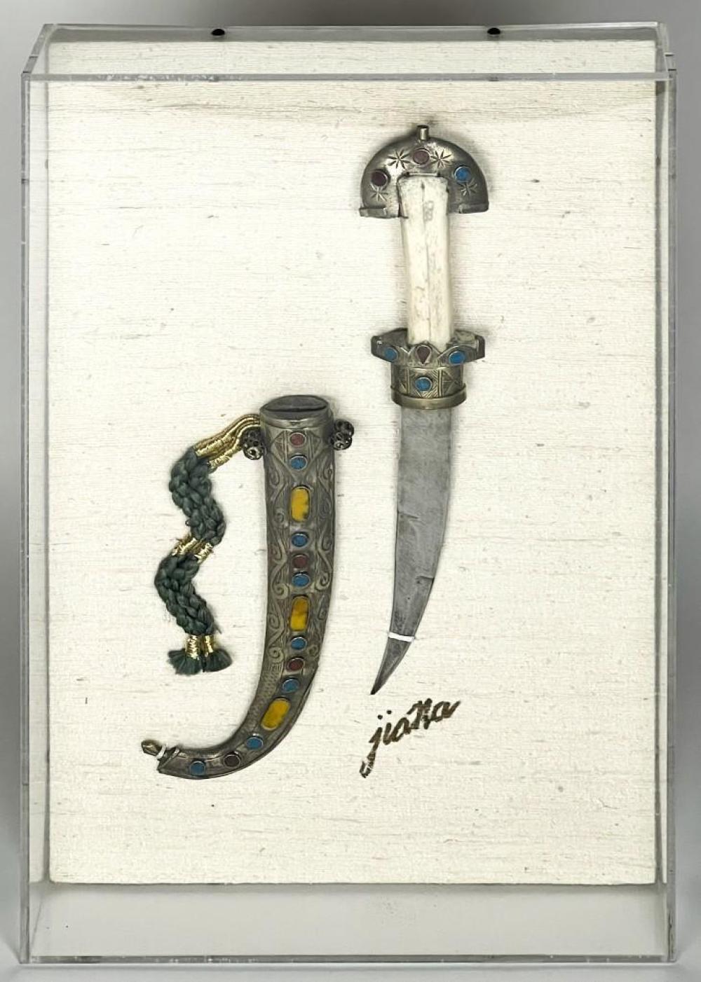 Antique dagger with curved scimitar-like blade and jeweled hilt and guard, displayed on a white background with a decorative beaded cord.