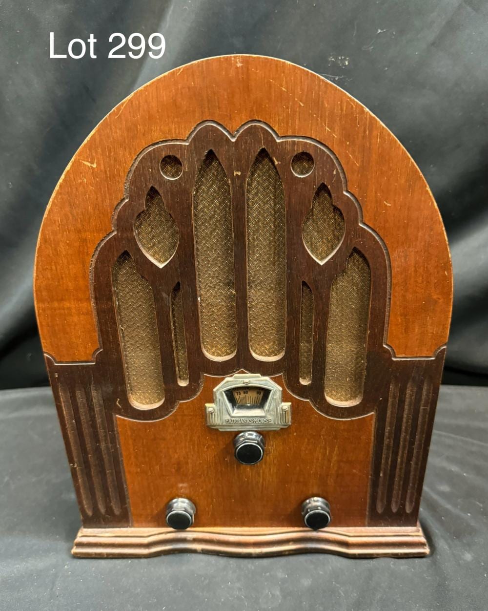 Front view of a vintage wooden tube radio cabinet with decorative grille panels, tuning scale window, and two knobs at the bottom.